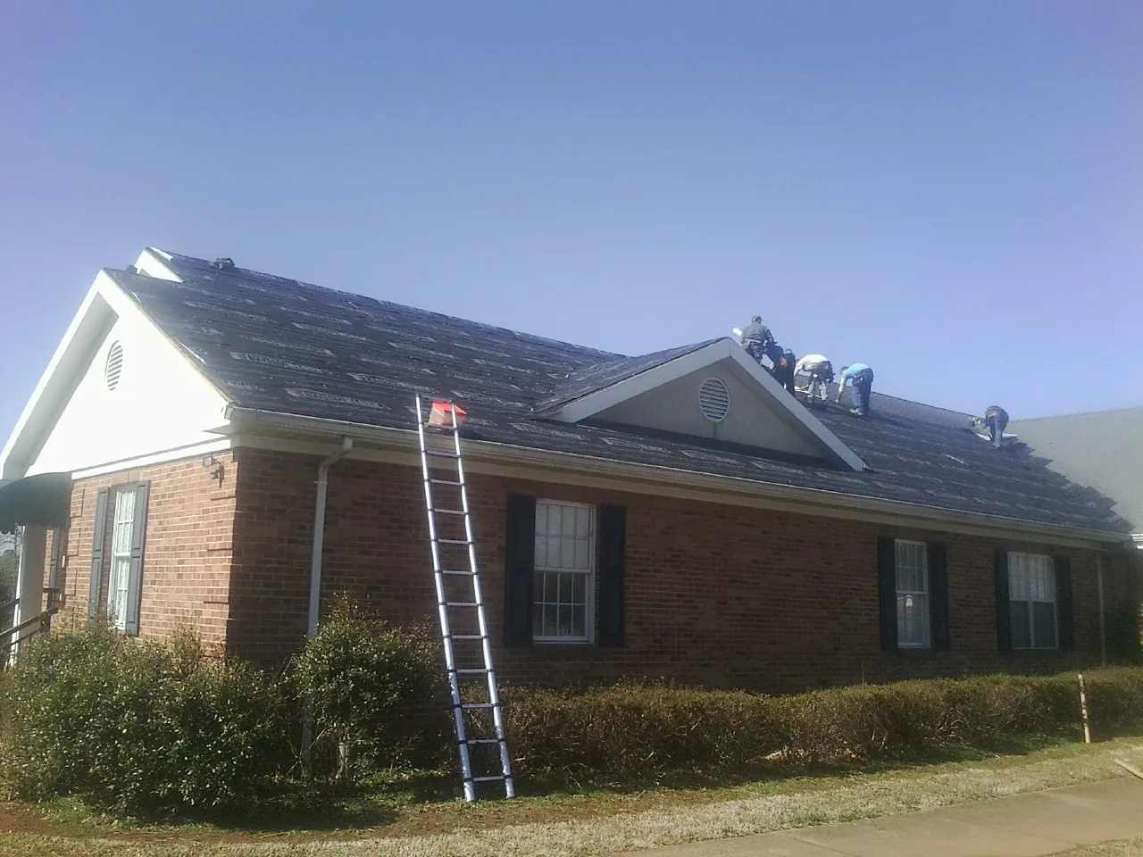 Crew tearing shingles off a brick ranch roof with a ladder set — Metal Roof Repair work by our crew in Herndon