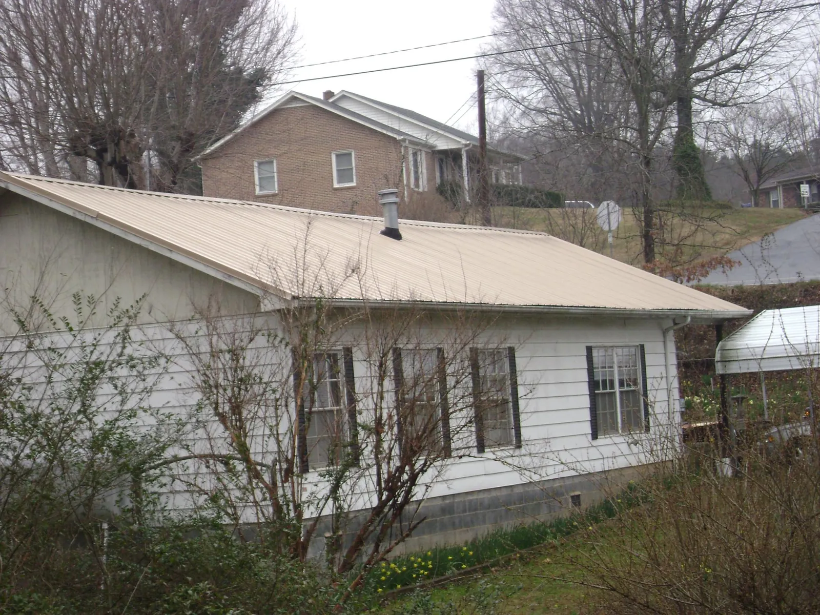 Tan metal roof on a white sided house set into a hillside — Commercial Roofing by Roofing Brothers in Herndon